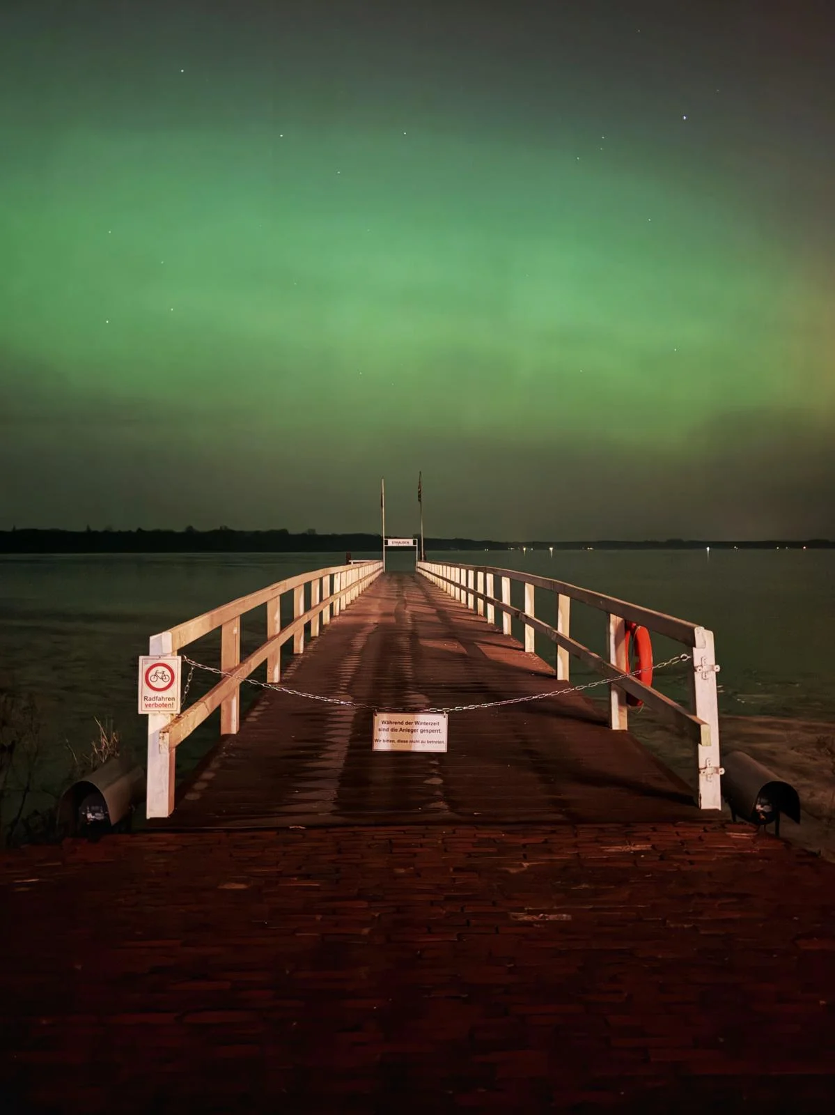 Der Steg in Eyhausen führt in den See unter leuchtend grünen Polarlichtern