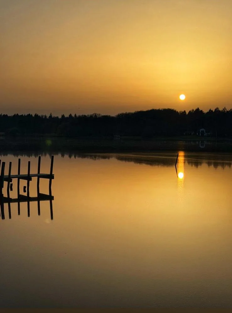 Goldener Sonnenuntergang über dem ruhigen See mit Holzsteg