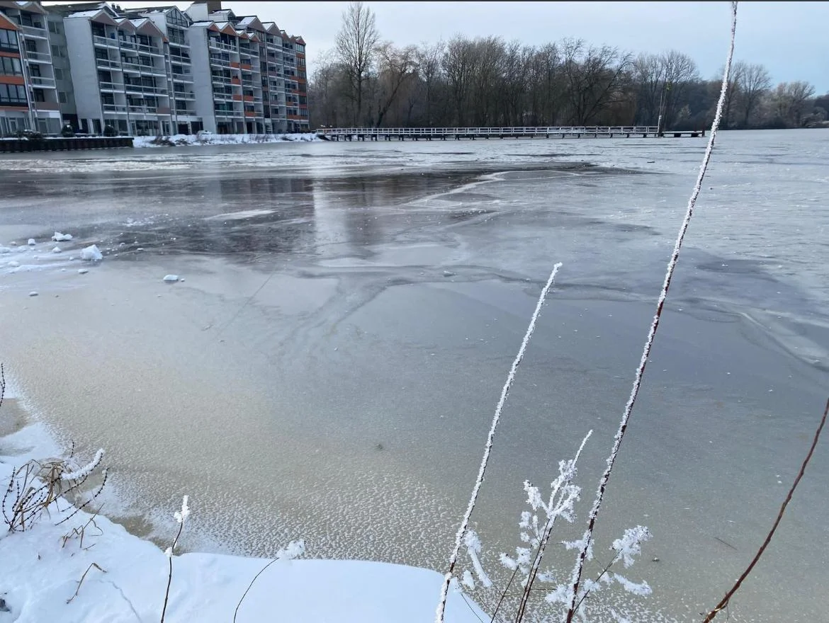 Blick über das eisige Ufer auf den zugefrorenen See und entfernte Gebäude