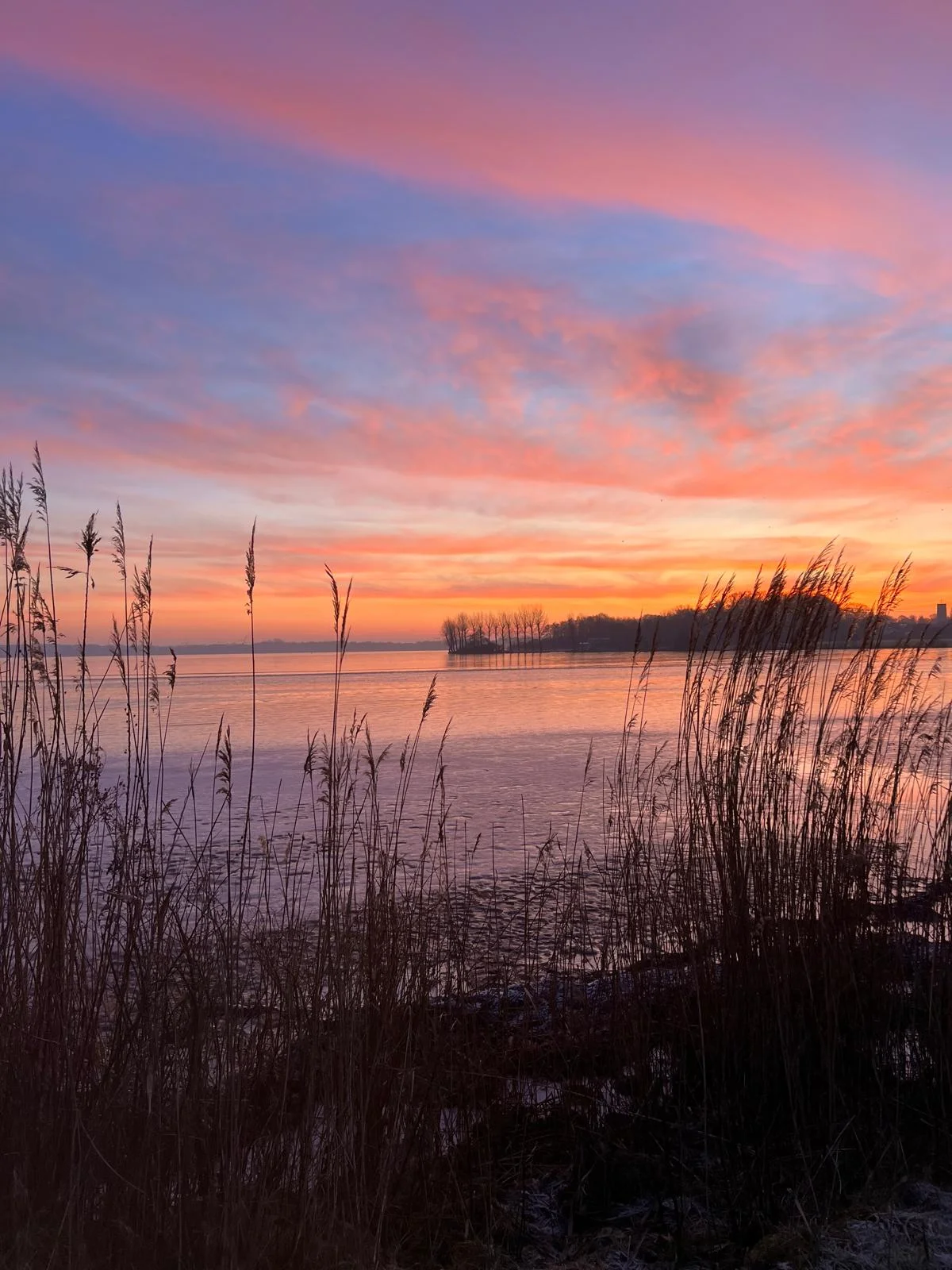 Romantischer Sonnenuntergang mit pinken Wolken über dem zugefrorenen See